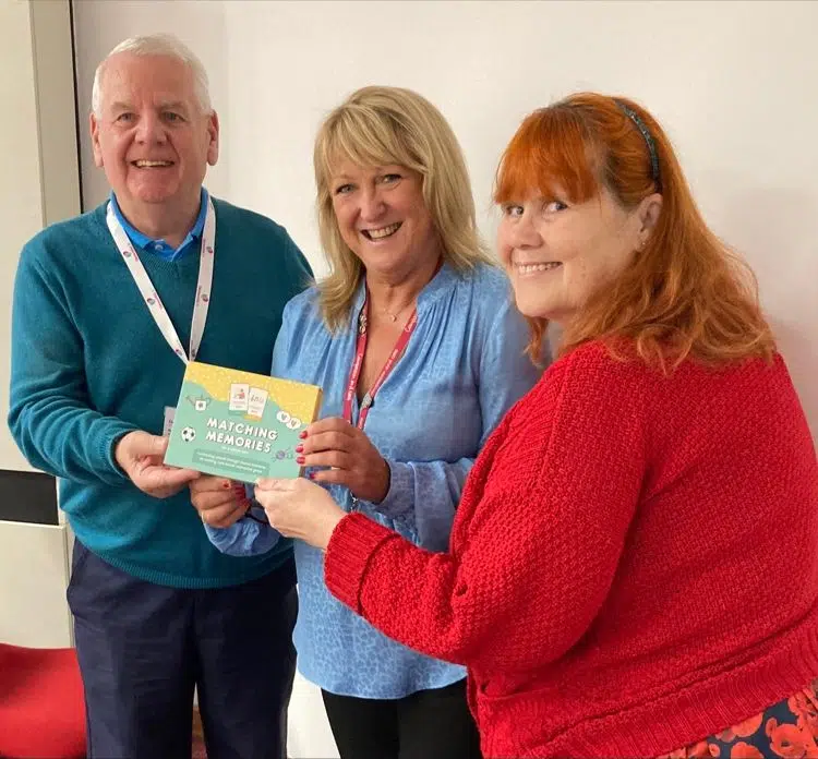 Three people holding an A Good Day Matching Memories game