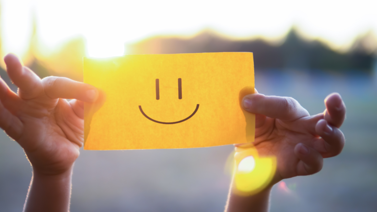 Smiley face on post-it note held up in the sunshine to show how living well with dementia is possible for all stages