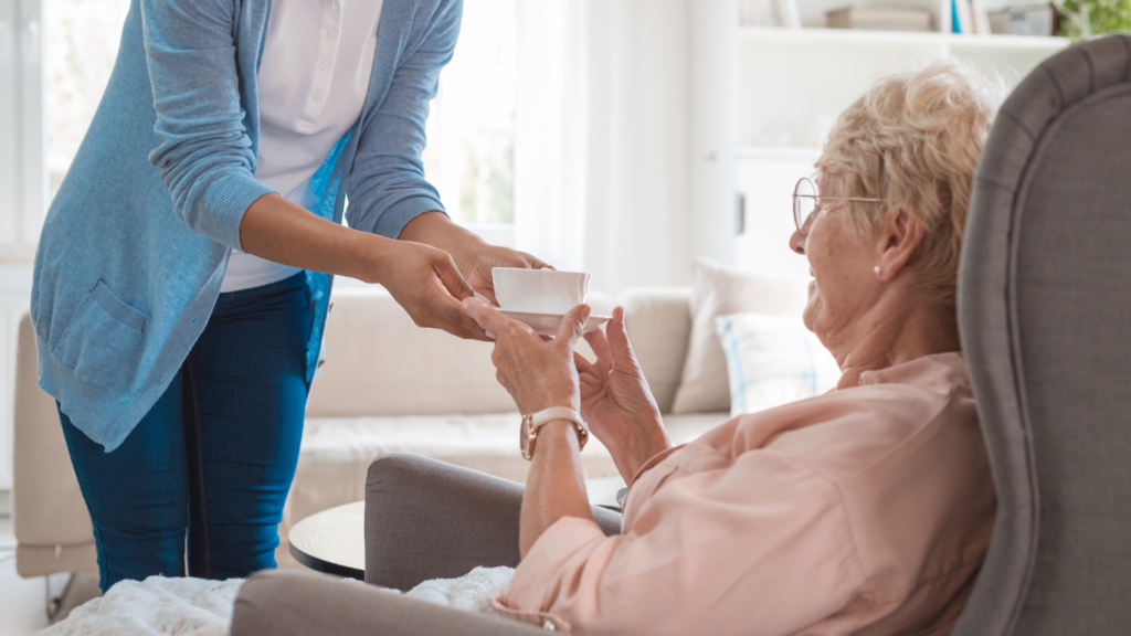older woman in care home being handed a warm drink as part of spring dementia tips for connection and conversation